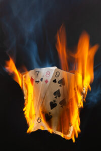 Bild des Monats September 2025 - „Heißes Kartenspiel“ Spielkarten stehen in lodernden Flammen, orangefarbene Glut und blauer Rauch kontrastieren mit dem dunklen Hintergrund.